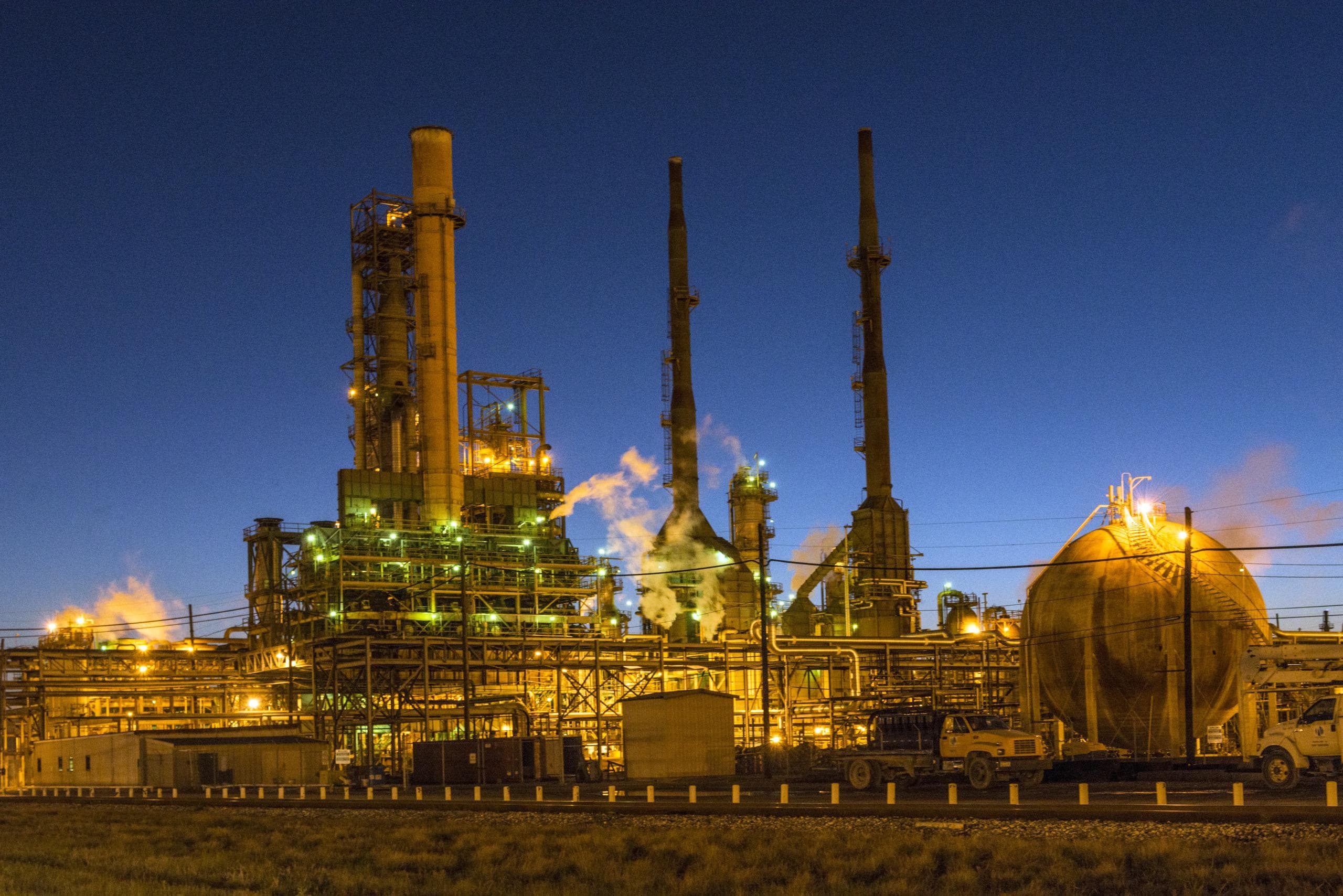 Refinery process towers and a spherical pressure vessel lit up at dusk in Port Arthur, Texas